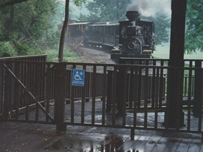 ©S.L.Reay photo of a train station in the rain with an old time steam engine and a few cars pulling into the station